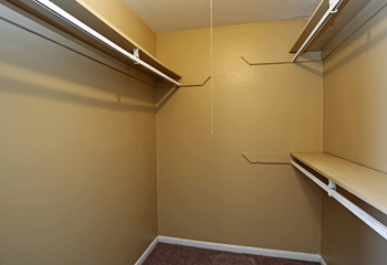 Walk in closet with one shelf on left and two on the right for hanging clothes.  Beige paint and carpet.